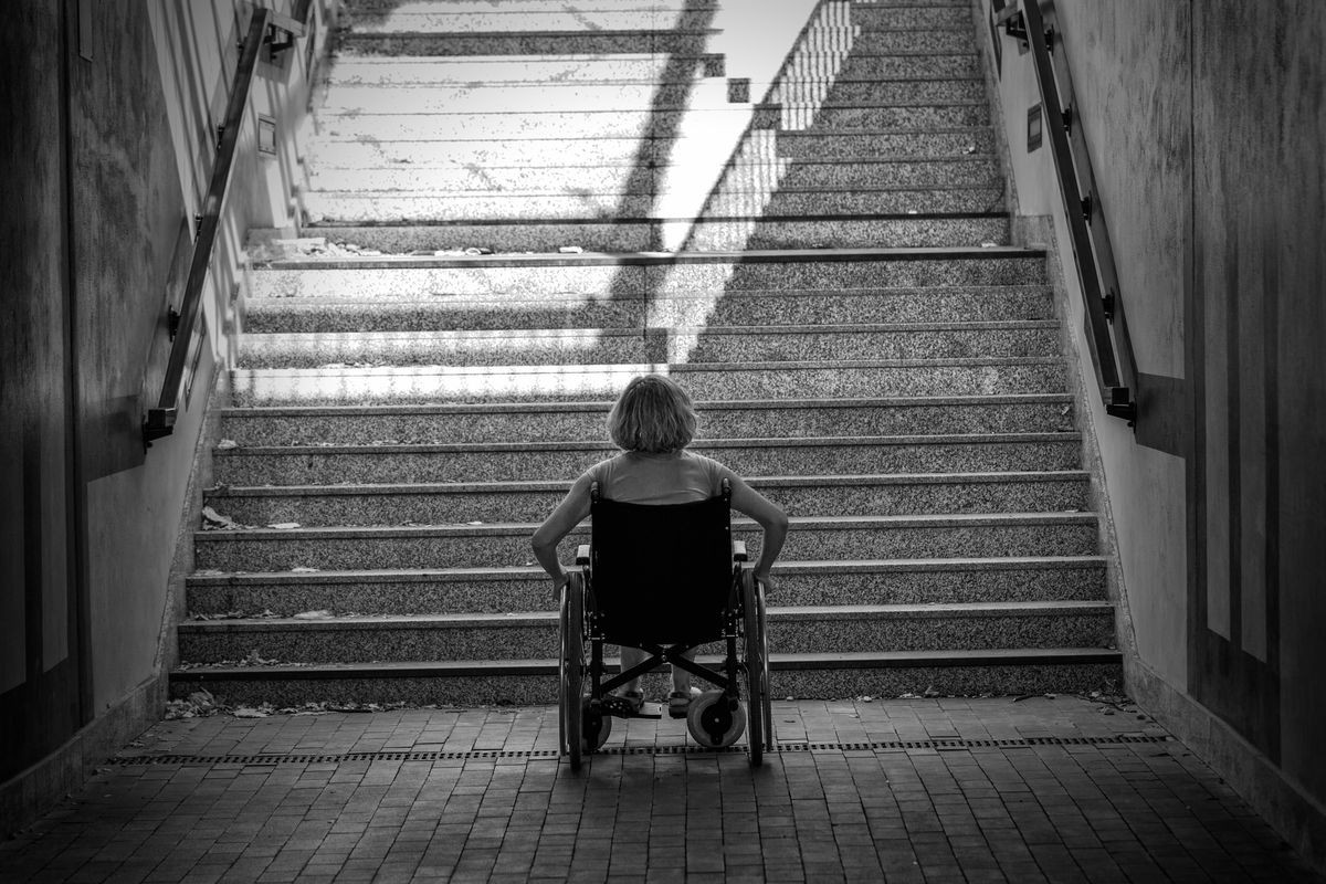 woman on wheelchair standing before stairs looking up for help